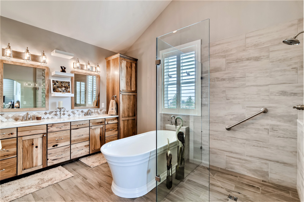 This is an example of a large rural ensuite bathroom in Denver with shaker cabinets, medium wood cabinets, a freestanding bath, a built-in shower, grey tiles, metro tiles, grey walls, wood-effect flooring, a submerged sink, quartz worktops, brown floors, a hinged door, white worktops, double sinks, a built in vanity unit and a vaulted ceiling.