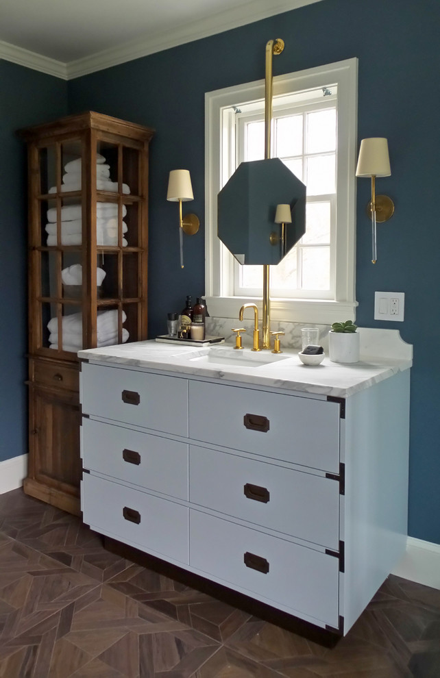 Inredning av ett klassiskt badrum, med vita skåp, blå väggar, ett undermonterad handfat, brunt golv och släta luckor