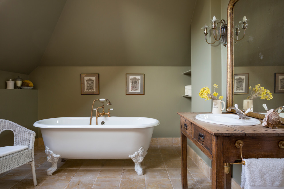 Cette image montre une salle de bain principale méditerranéenne en bois foncé de taille moyenne avec un mur vert, un sol en travertin, une baignoire sur pieds, un lavabo posé, un plan de toilette en bois, un sol beige, un plan de toilette marron et un placard à porte plane.