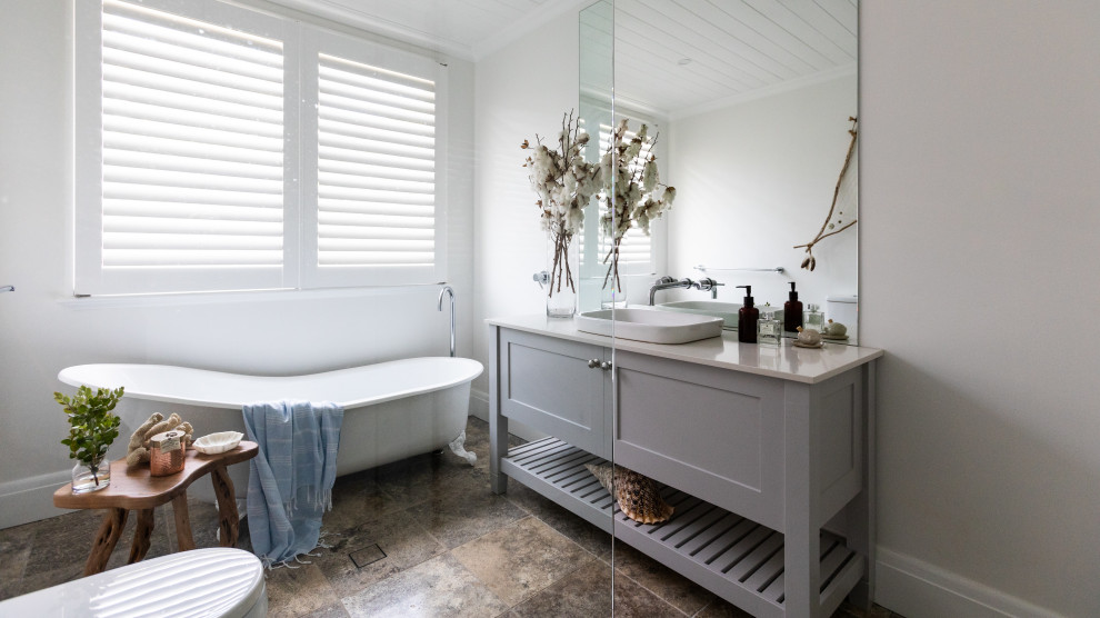 На фото: ванная комната среднего размера в стиле кантри с серыми фасадами, ванной на ножках, угловым душем, белыми стенами, коричневым полом, душем с распашными дверями, бежевой столешницей и тумбой под одну раковину