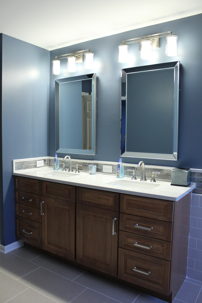 Exemple d'une salle de bain principale chic en bois foncé de taille moyenne avec un placard avec porte à panneau surélevé, un carrelage métro, un plan de toilette en quartz modifié, un plan de toilette blanc, une douche d'angle, un carrelage gris, un mur bleu, une cabine de douche à porte battante, une baignoire posée, un sol en carrelage de porcelaine, un lavabo encastré et un sol gris.