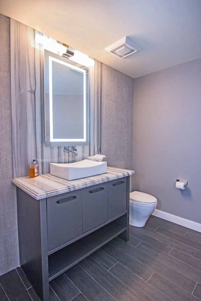 Cette image montre une petite salle d'eau design avec un placard à porte plane, des portes de placard grises, WC à poser, un carrelage noir et blanc, du carrelage en marbre, un mur violet, un sol en carrelage de céramique, une vasque, un plan de toilette en marbre et un sol gris.