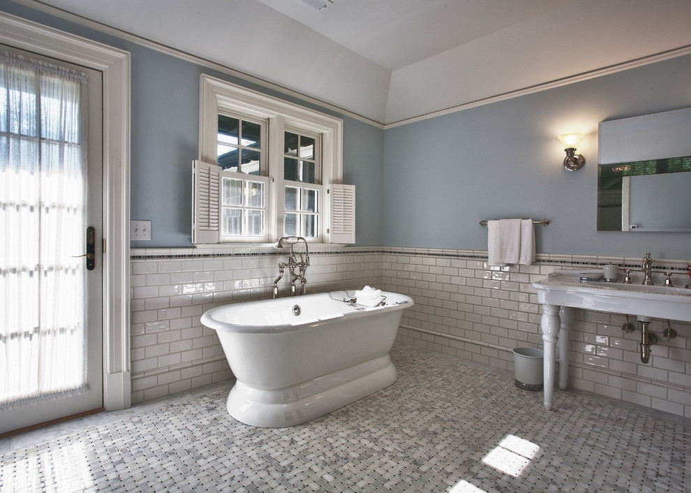 Foto på ett stort vintage badrum, med ett konsol handfat, ett fristående badkar, en dubbeldusch, en toalettstol med hel cisternkåpa, vit kakel, porslinskakel, blå väggar och marmorgolv