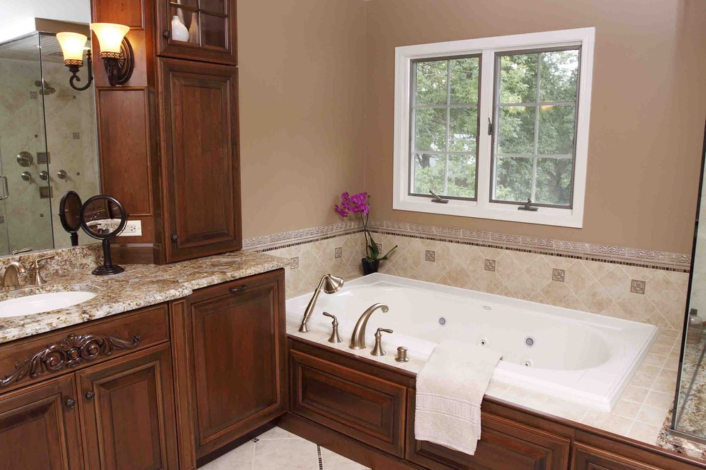 Foto di una stanza da bagno padronale chic di medie dimensioni con lavabo sottopiano, ante con bugna sagomata, ante in legno bruno, top in granito, vasca da incasso, piastrelle beige e pareti beige