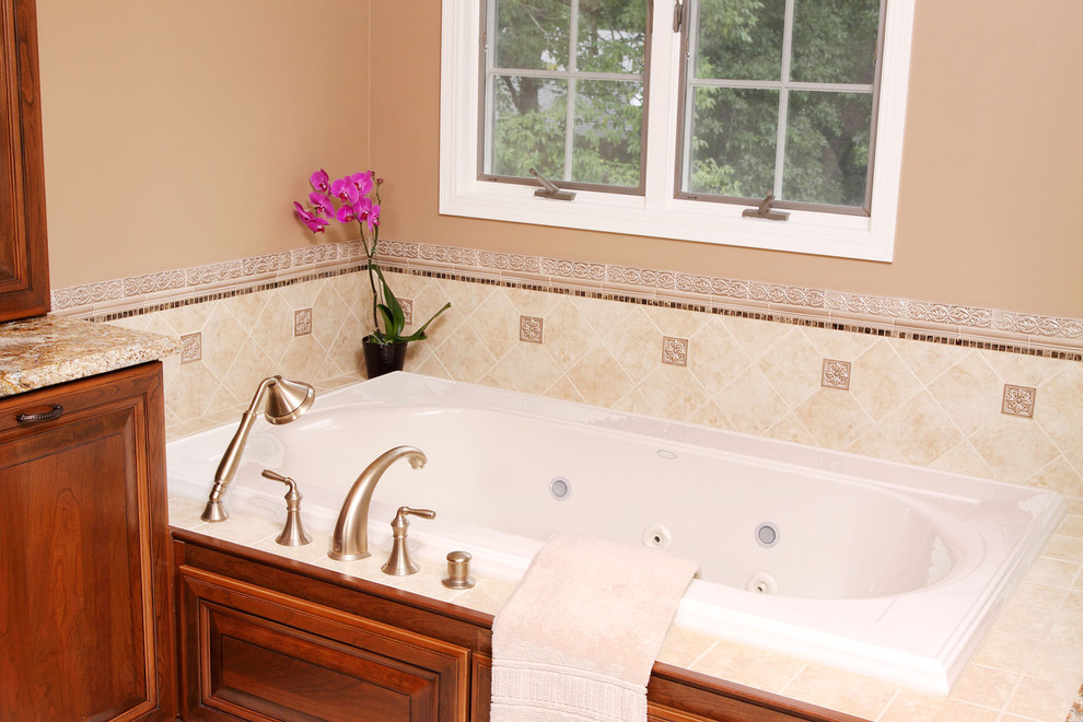 Example of a mid-sized classic master beige tile drop-in bathtub design in Chicago with raised-panel cabinets, medium tone wood cabinets, granite countertops and beige walls
