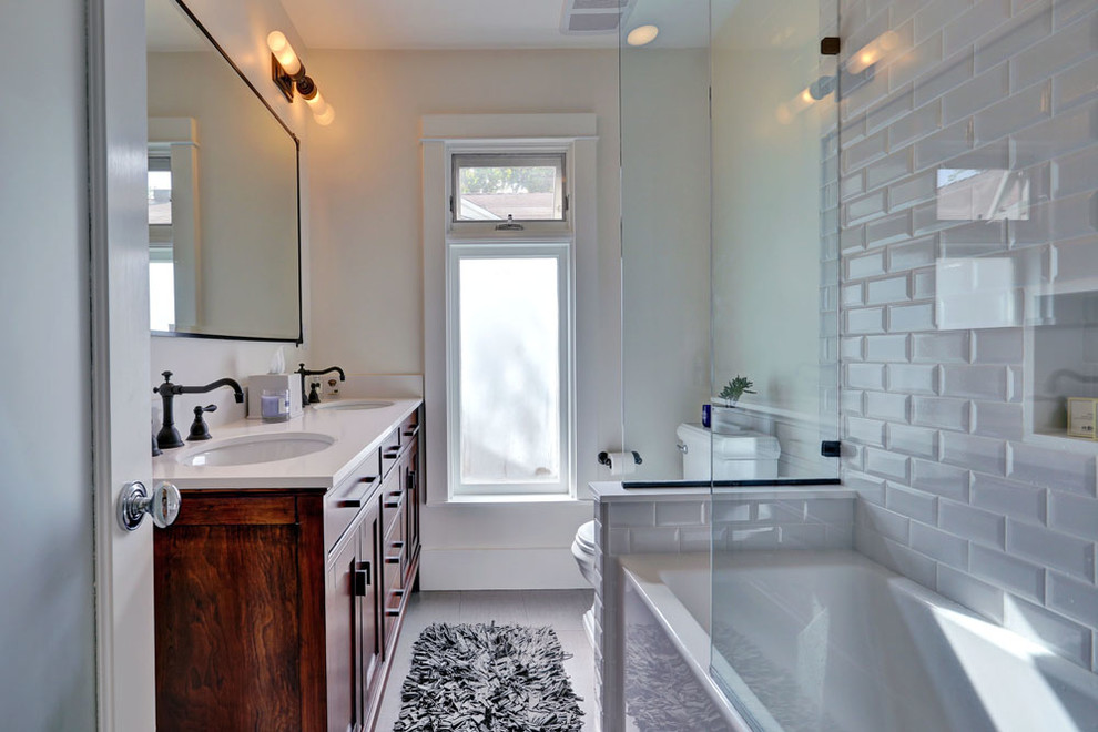 Inspiration for a medium sized classic ensuite bathroom in Los Angeles with shaker cabinets, dark wood cabinets, an alcove bath, a shower/bath combination, a one-piece toilet, white tiles, metro tiles, white walls, porcelain flooring, a submerged sink, solid surface worktops, grey floors and an open shower.