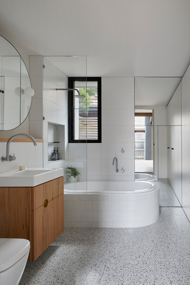 Idéer för ett mellanstort modernt vit badrum med dusch, med släta luckor, skåp i mellenmörkt trä, ett platsbyggt badkar, en dusch/badkar-kombination, en toalettstol med hel cisternkåpa, vit kakel, porslinskakel, vita väggar, med dusch som är öppen, ett konsol handfat och grått golv