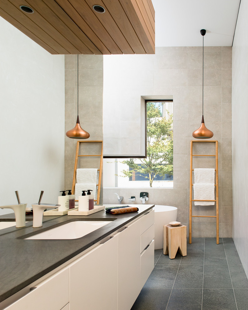 Idee per una stanza da bagno minimal con ante lisce, ante bianche, vasca freestanding, piastrelle grigie, pareti grigie, lavabo sottopiano, pavimento grigio e top grigio