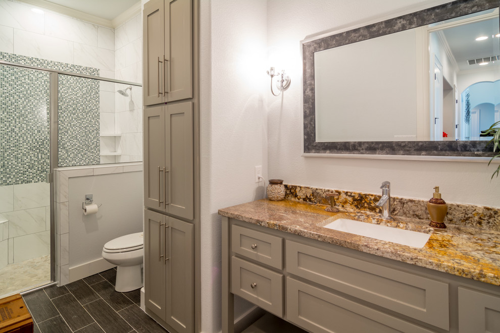 Inredning av ett klassiskt badrum, med luckor med infälld panel, grå skåp, en toalettstol med separat cisternkåpa, brun kakel, keramikplattor, grå väggar, klinkergolv i keramik, ett undermonterad handfat och granitbänkskiva