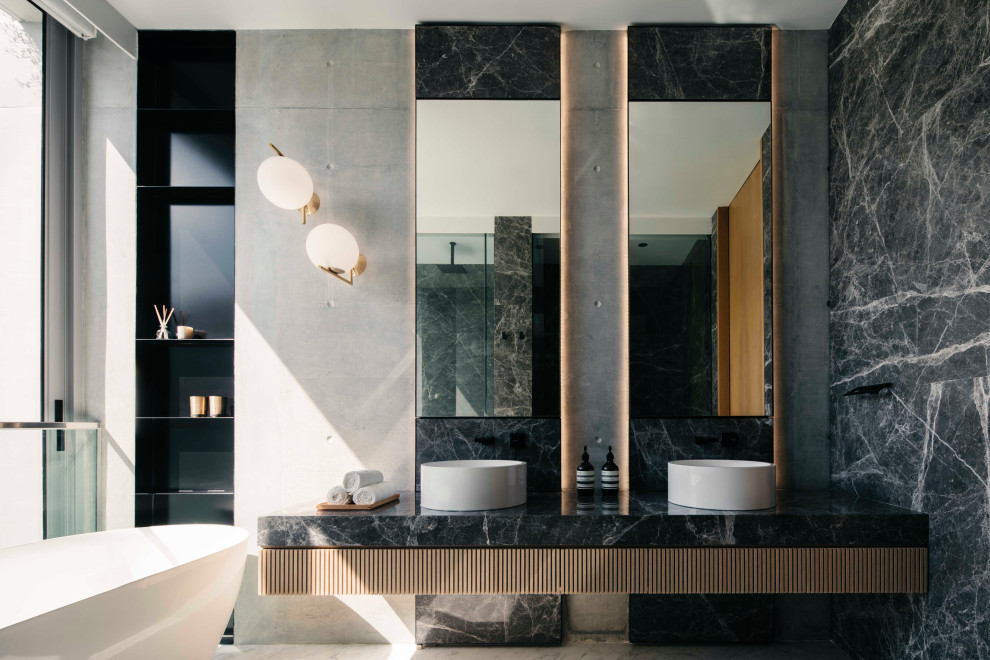 Réalisation d'une salle de bain design avec une baignoire indépendante, un carrelage gris, un mur gris, une vasque, un sol gris, un plan de toilette noir, meuble double vasque et meuble-lavabo suspendu.