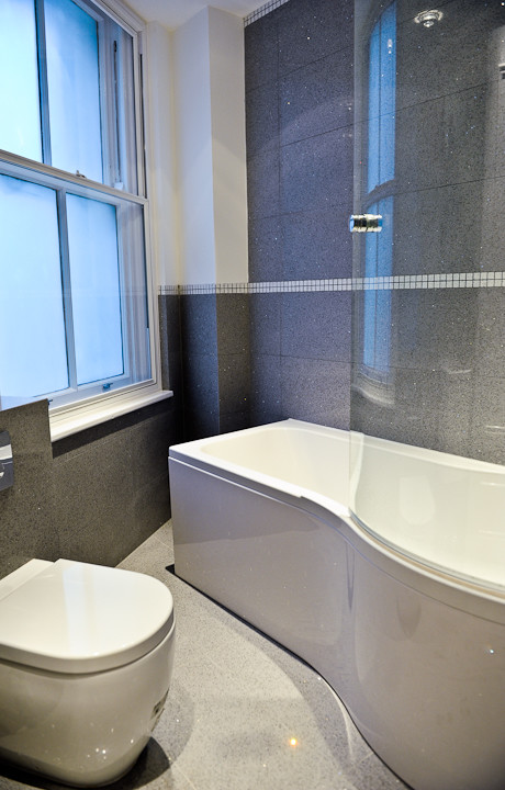 This is an example of a small modern ensuite bathroom in London with an integrated sink, a built-in bath, a shower/bath combination, a one-piece toilet, grey tiles, ceramic tiles, grey walls and ceramic flooring.