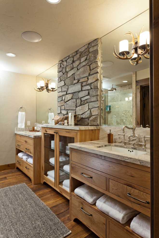 Idées déco pour une salle de bain principale montagne en bois brun avec un placard à porte plane, un mur beige, parquet foncé, un lavabo encastré, un sol marron et un mur en pierre.