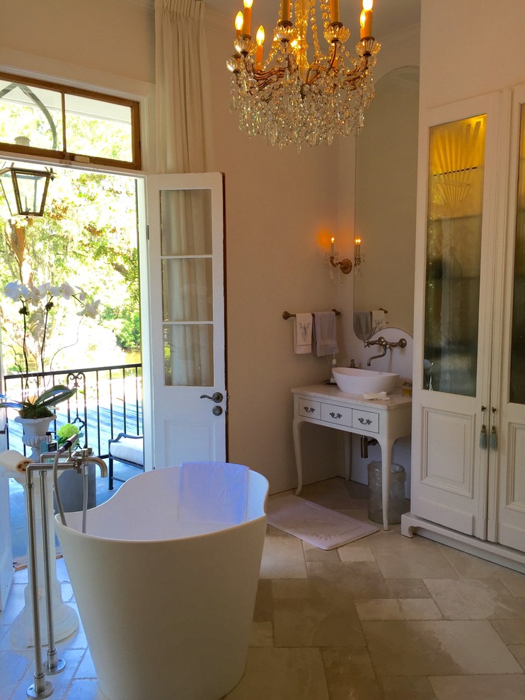 Example of a large classic master travertine floor freestanding bathtub design in New Orleans with furniture-like cabinets, white cabinets and a vessel sink