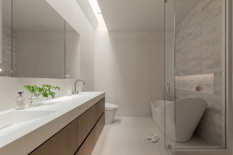 Стильный дизайн: главная ванная комната в современном стиле с плоскими фасадами, коричневыми фасадами, отдельно стоящей ванной, серой плиткой, монолитной раковиной, белой столешницей, тумбой под две раковины и подвесной тумбой - последний тренд