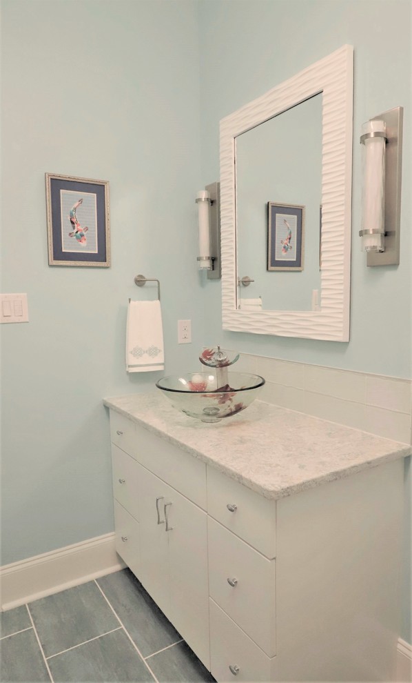 Inredning av ett maritimt mellanstort flerfärgad flerfärgat badrum med dusch, med luckor med infälld panel, vita skåp, en hörndusch, en toalettstol med separat cisternkåpa, vit kakel, glaskakel, blå väggar, klinkergolv i porslin, ett fristående handfat, bänkskiva i akrylsten, blått golv och dusch med skjutdörr