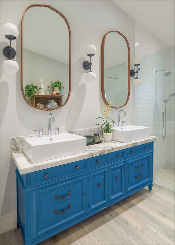 Exemple d'une douche en alcôve bord de mer avec un placard avec porte à panneau encastré, des portes de placard bleues, un carrelage blanc, un mur blanc, parquet clair, une vasque, un sol beige, un plan de toilette blanc, meuble double vasque et meuble-lavabo sur pied.