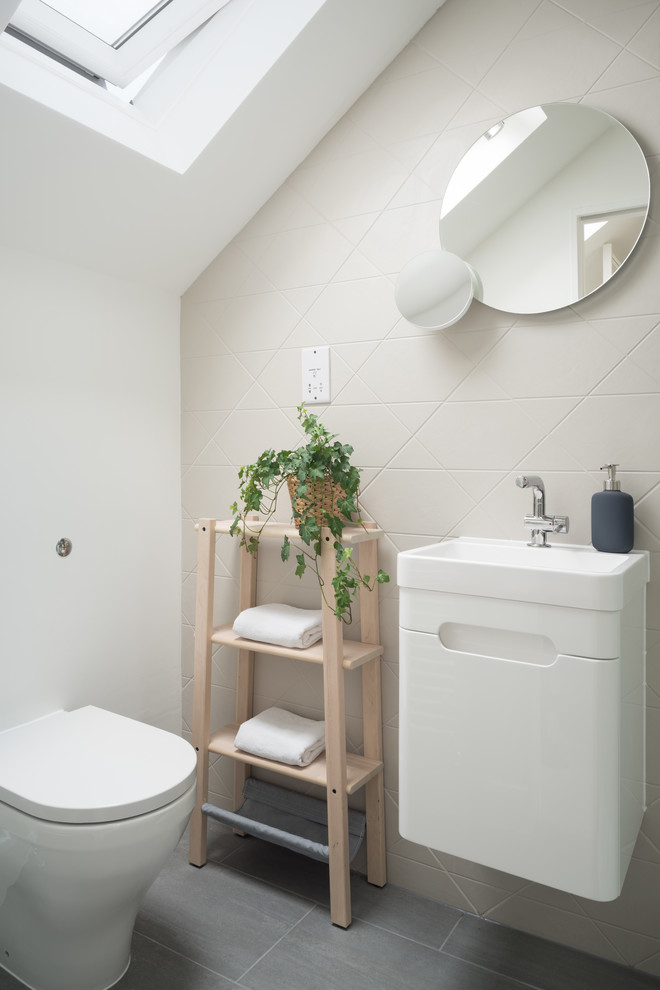 На фото: ванная комната в скандинавском стиле с плоскими фасадами, белыми фасадами, унитазом-моноблоком, бежевой плиткой, белыми стенами, душевой кабиной, подвесной раковиной и серым полом