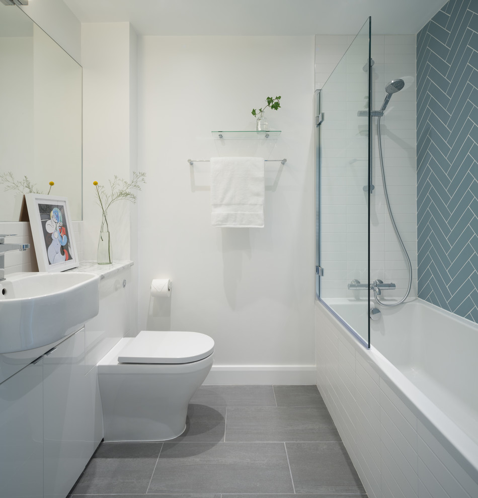 Inspiration for a scandinavian shower room bathroom in London with flat-panel cabinets, white cabinets, an alcove bath, a shower/bath combination, a one-piece toilet, blue tiles, white walls, a built-in sink, marble worktops, grey floors, an open shower and grey worktops.