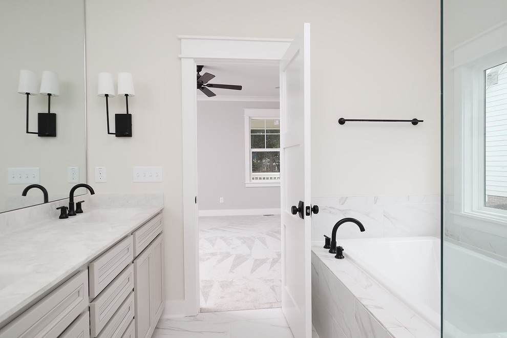 Photo of a large classic ensuite bathroom in Raleigh with recessed-panel cabinets, grey cabinets, an alcove bath, an alcove shower, a two-piece toilet, grey tiles, ceramic tiles, beige walls, ceramic flooring, an integrated sink, marble worktops, grey floors, a hinged door and multi-coloured worktops.