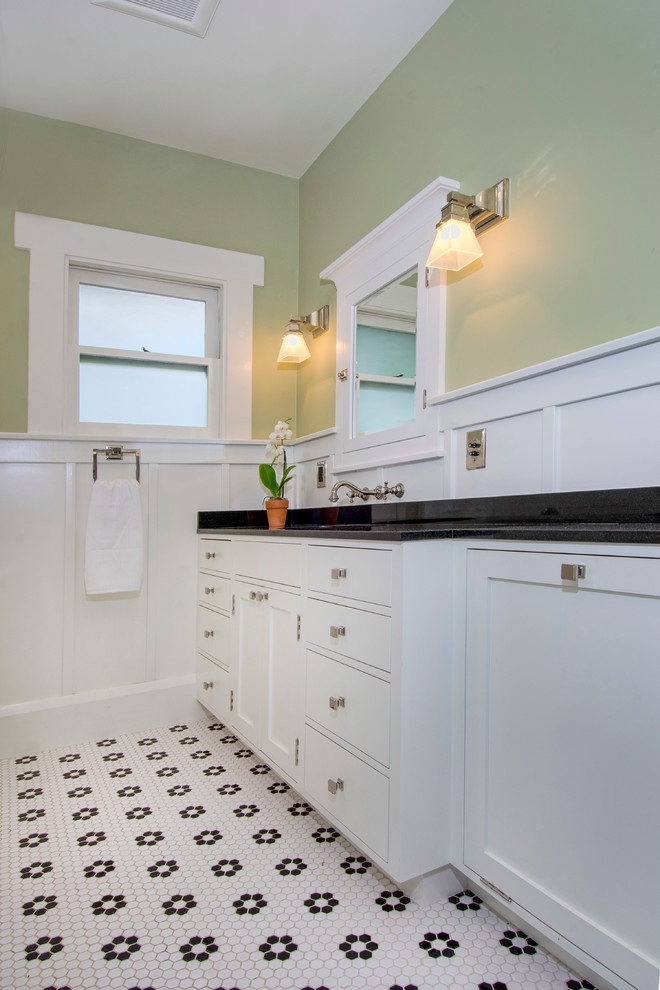 Cette photo montre une salle de bain craftsman avec un placard à porte shaker, des portes de placard blanches, un mur vert, un sol en carrelage de céramique, un lavabo encastré, un plan de toilette en granite, un sol blanc et un plan de toilette noir.