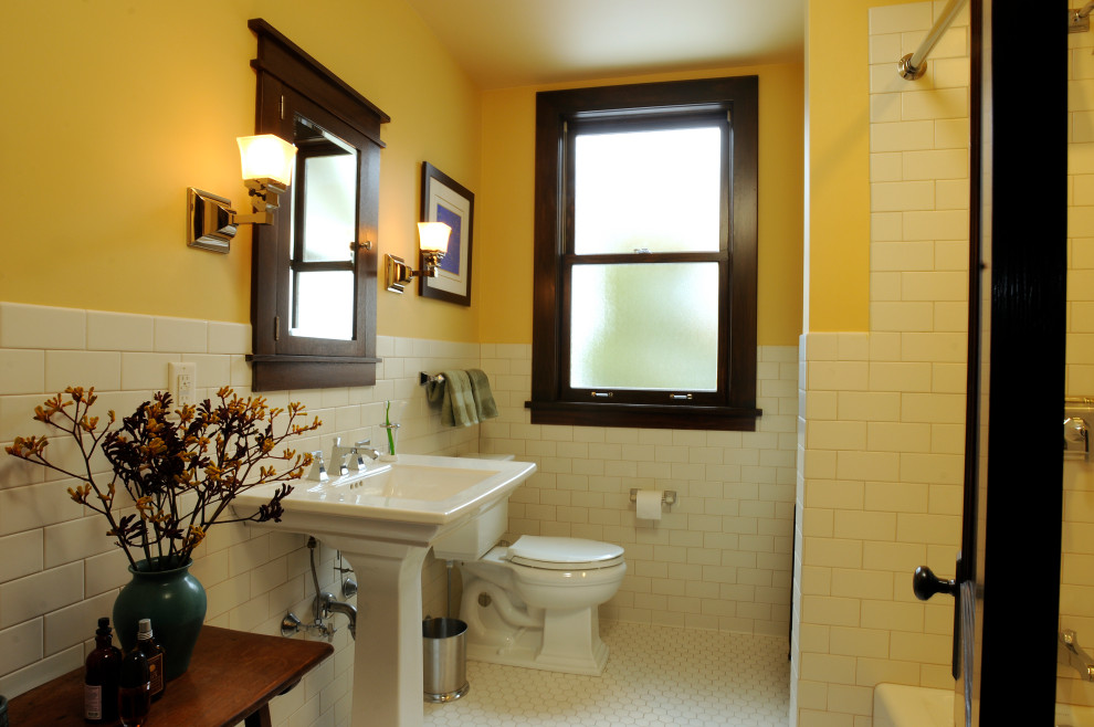 Inredning av ett amerikanskt badrum, med en toalettstol med separat cisternkåpa, tunnelbanekakel, gula väggar, klinkergolv i porslin, ett piedestal handfat och vitt golv