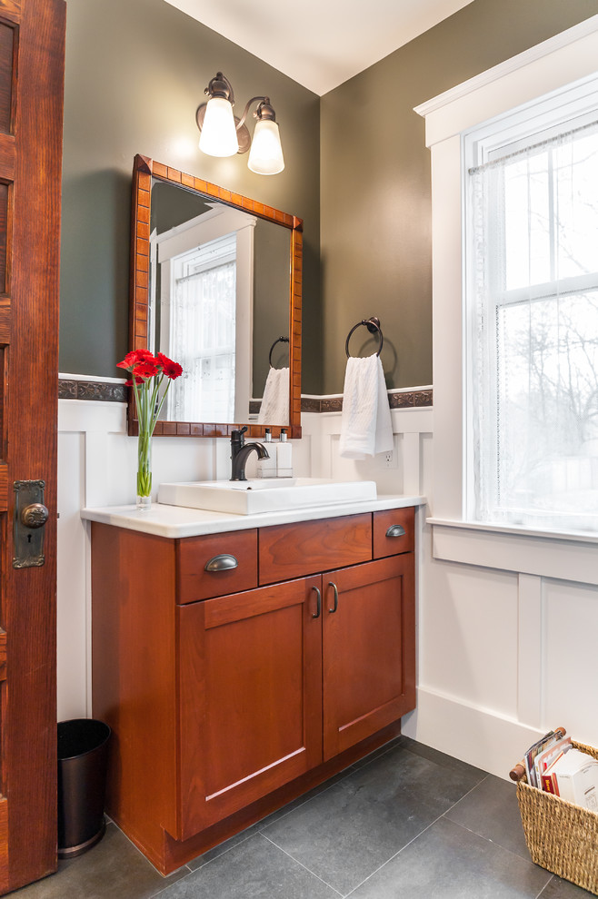 Cette image montre une petite salle d'eau craftsman en bois brun avec un placard à porte shaker, un carrelage blanc, un carrelage métro, un mur vert, une vasque, un plan de toilette en surface solide, une cabine de douche à porte battante et un plan de toilette blanc.