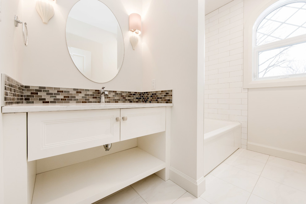 На фото: большая ванная комната в стиле кантри с белыми фасадами, ванной в нише, бежевой плиткой, керамогранитной плиткой, полом из керамогранита, столешницей из кварцита, врезной раковиной и белыми стенами с