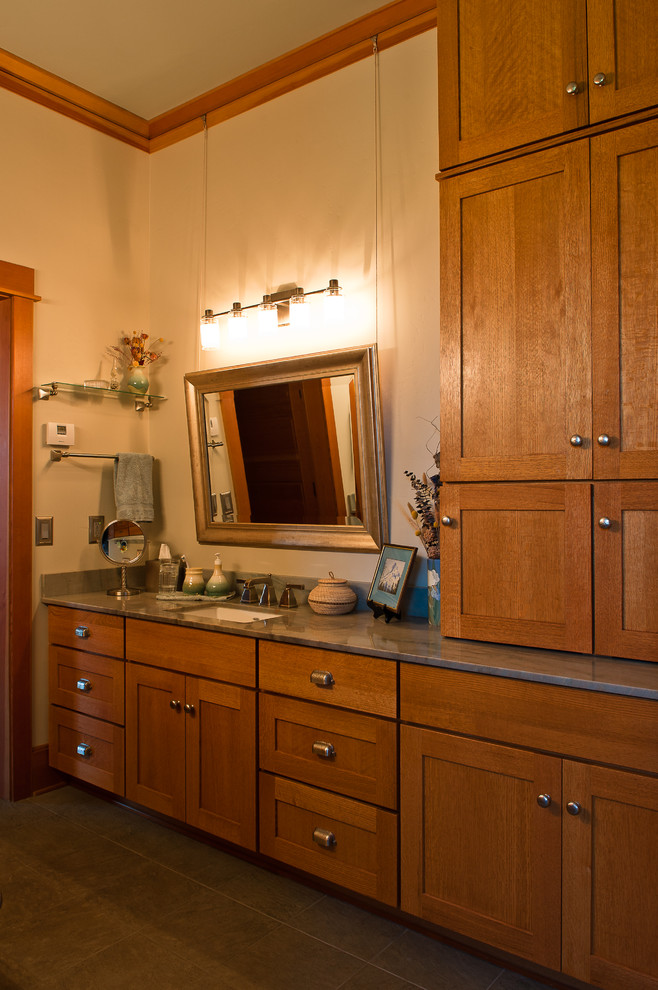 Aménagement d'une salle de bain principale craftsman en bois brun de taille moyenne avec un placard à porte shaker, un mur beige, un sol en carrelage de porcelaine, un lavabo encastré et un plan de toilette en granite.