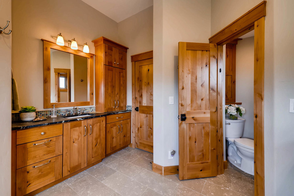 Photo of a large classic ensuite bathroom in Denver with shaker cabinets, medium wood cabinets, a freestanding bath, a corner shower, a two-piece toilet, beige tiles, mosaic tiles, beige walls, limestone flooring, a submerged sink, soapstone worktops, grey floors and a hinged door.