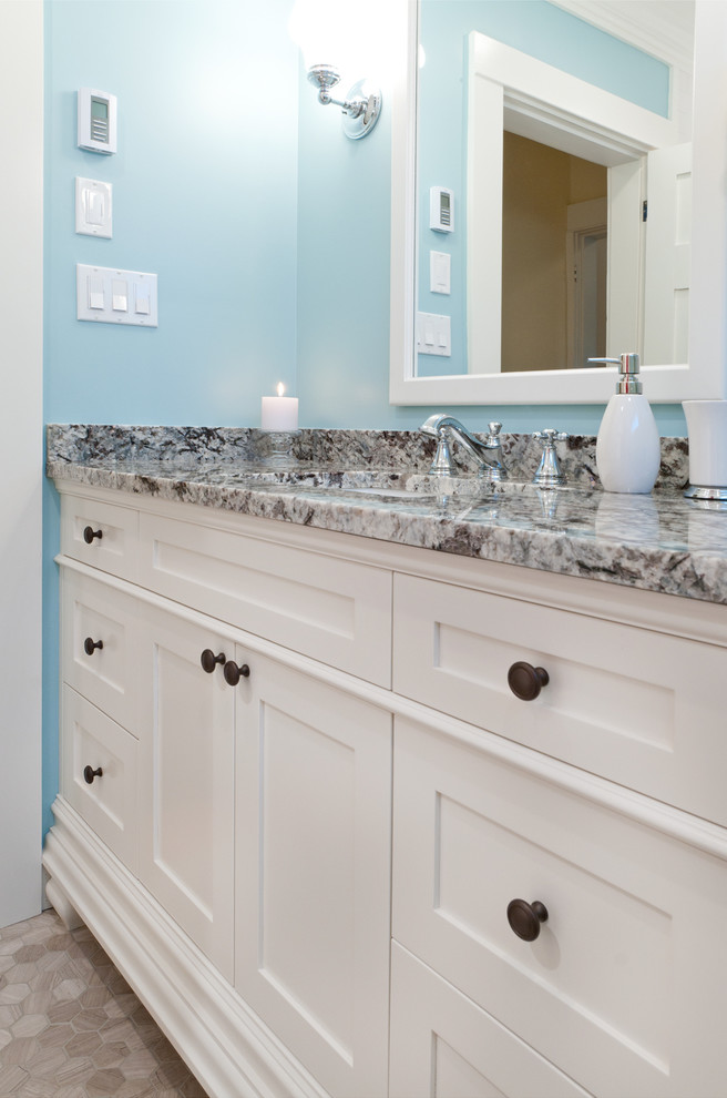 Amerikansk inredning av ett litet badrum med dusch, med ett undermonterad handfat, skåp i shakerstil, vita skåp, granitbänkskiva, ett badkar i en alkov, en dusch/badkar-kombination, en toalettstol med separat cisternkåpa, flerfärgad kakel, stenhäll, blå väggar och klinkergolv i keramik