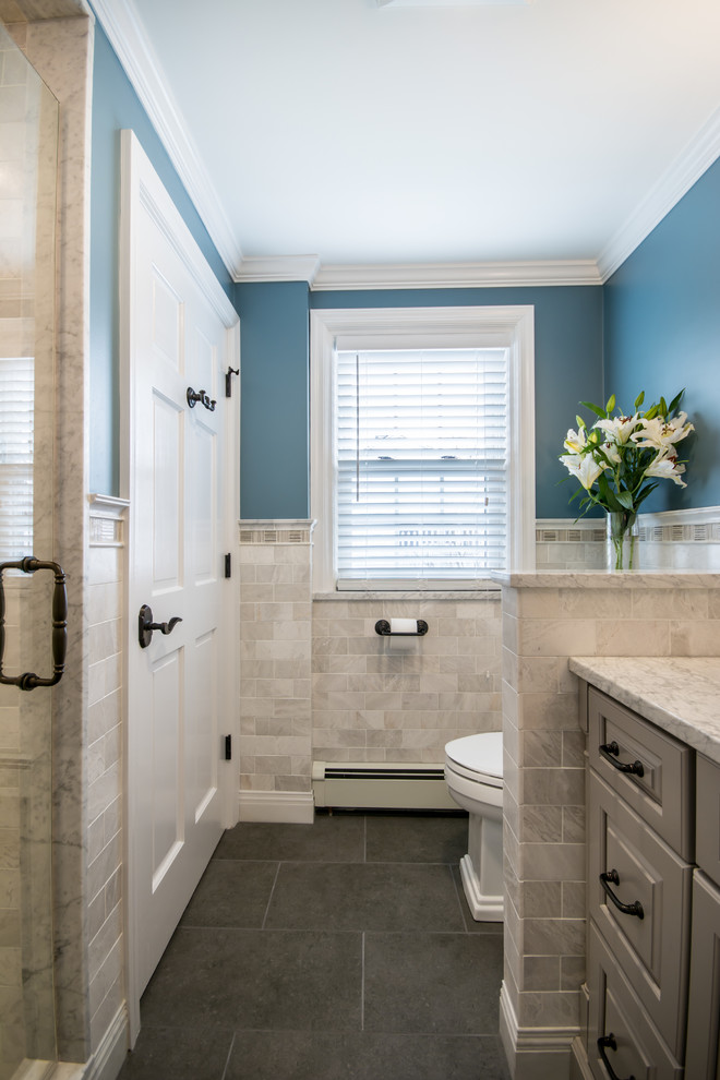 Cette photo montre une salle de bain chic de taille moyenne avec un placard avec porte à panneau surélevé, des portes de placard grises, WC séparés, un carrelage blanc, un carrelage métro, un mur bleu, un sol en carrelage de porcelaine, un lavabo encastré et un plan de toilette en marbre.