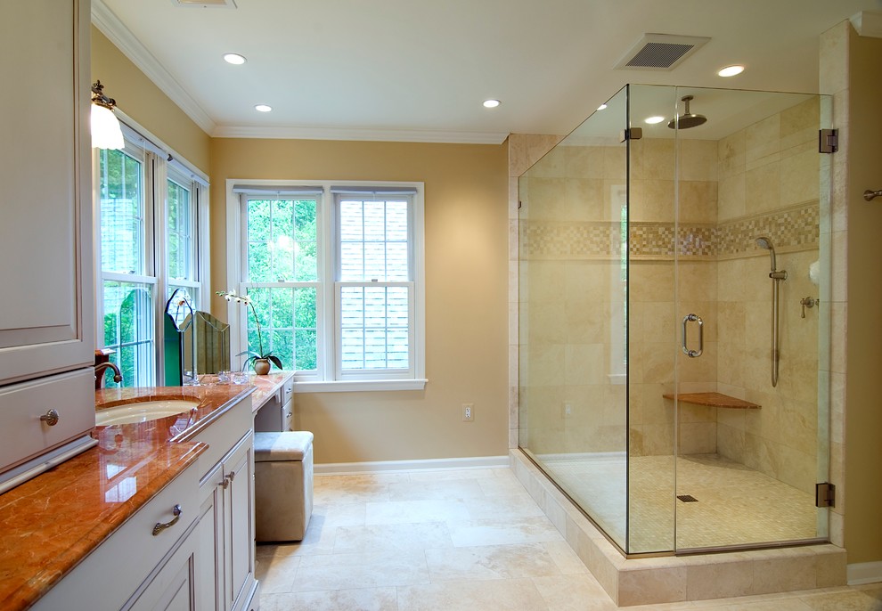 Diseño de cuarto de baño tradicional con lavabo bajoencimera, armarios con paneles con relieve, puertas de armario grises, ducha esquinera y baldosas y/o azulejos beige