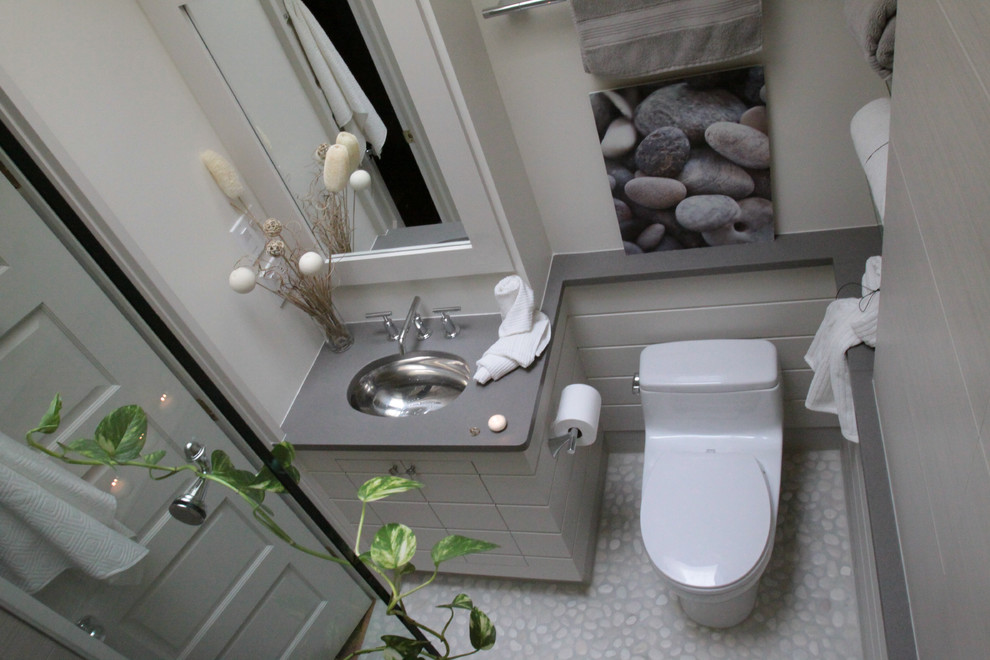 Modern inredning av ett mellanstort en-suite badrum, med möbel-liknande, grå skåp, en toalettstol med hel cisternkåpa, grå väggar, klinkergolv i småsten, ett undermonterad handfat, bänkskiva i rostfritt stål och en dusch i en alkov