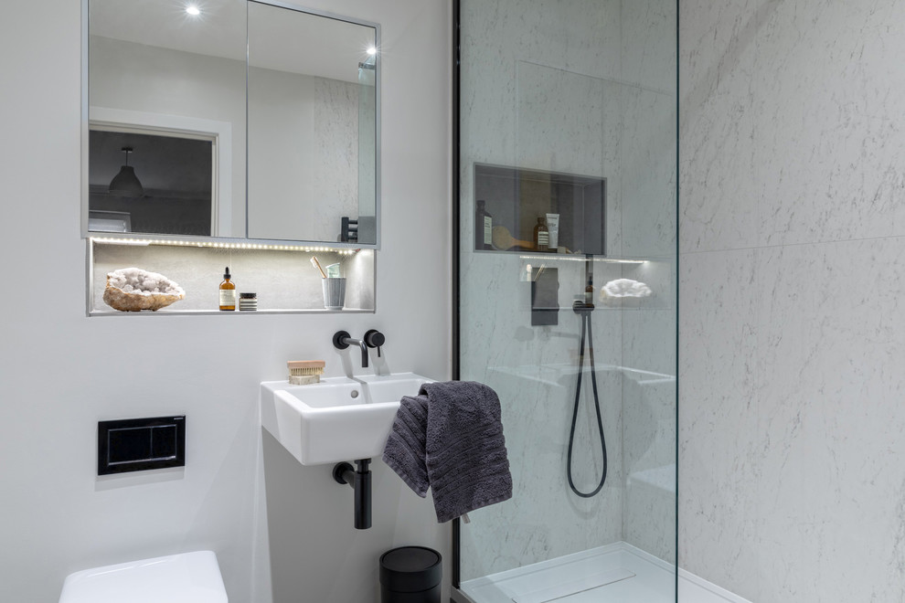 Minimalistisk inredning av ett litet en-suite badrum, med ett platsbyggt badkar, en öppen dusch, en vägghängd toalettstol, vit kakel, porslinskakel, vita väggar, klinkergolv i porslin, ett väggmonterat handfat och grått golv
