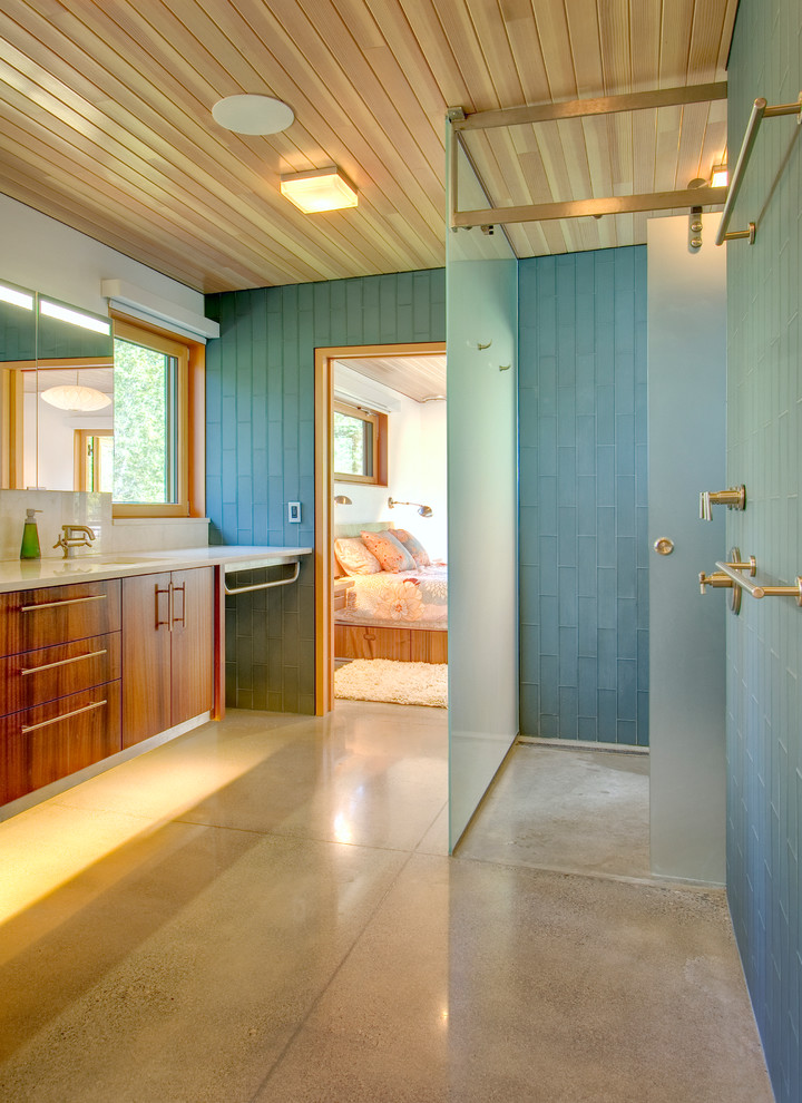 Example of a large trendy master blue tile and glass tile concrete floor corner shower design in Seattle with flat-panel cabinets, medium tone wood cabinets, white walls, an undermount sink and solid surface countertops