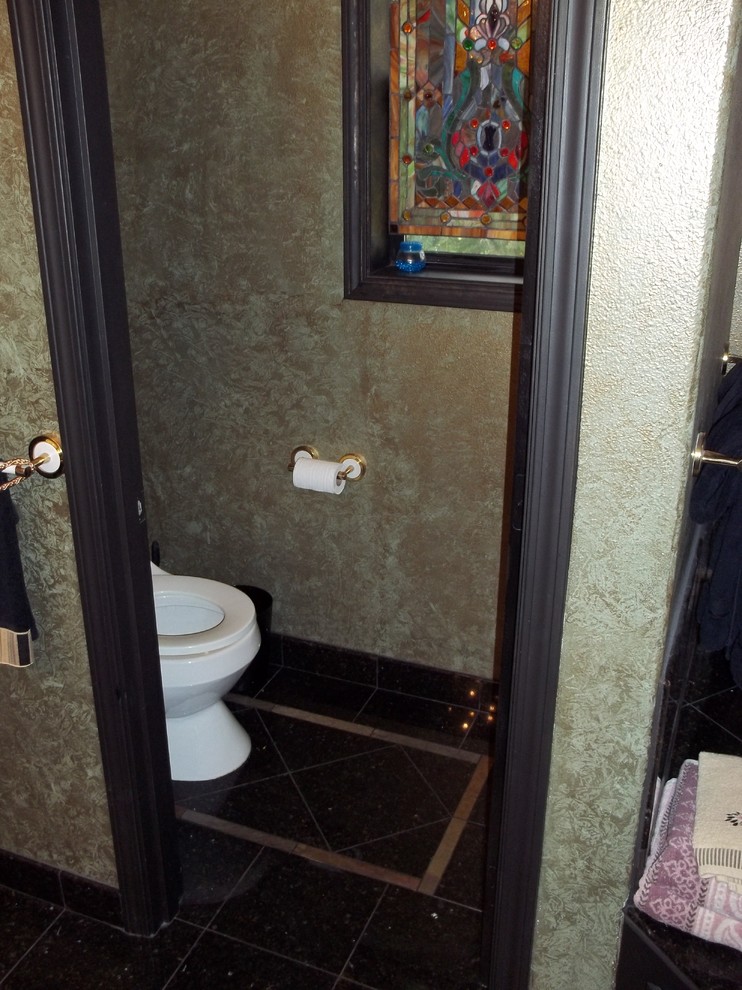 Modelo de cuarto de baño principal clásico de tamaño medio con lavabo encastrado, armarios con paneles con relieve, puertas de armario negras, encimera de granito, bañera encastrada, ducha esquinera, sanitario de dos piezas, baldosas y/o azulejos negros, baldosas y/o azulejos de piedra y paredes verdes