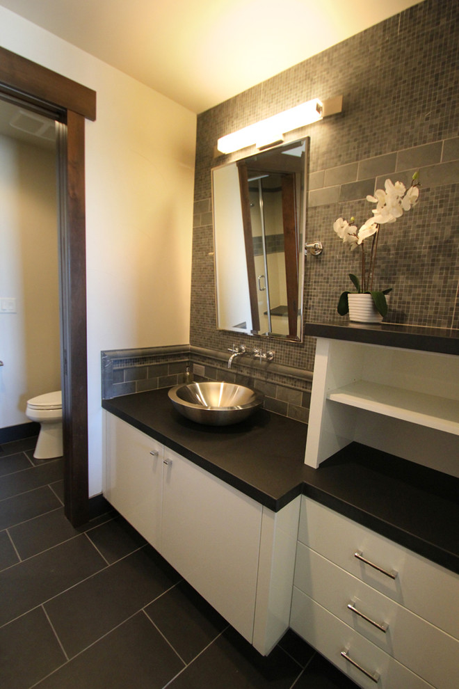 Idée de décoration pour une salle de bain design de taille moyenne avec un placard à porte plane, des portes de placard blanches, un carrelage gris, mosaïque, un mur beige, une vasque et un plan de toilette en surface solide.
