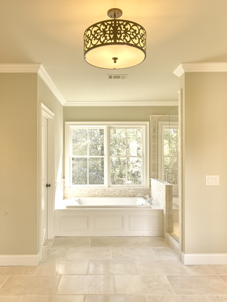Cette image montre une salle de bain avec des portes de placard blanches, une baignoire en alcôve, un mur beige, un sol en marbre, un carrelage beige et un carrelage de pierre.