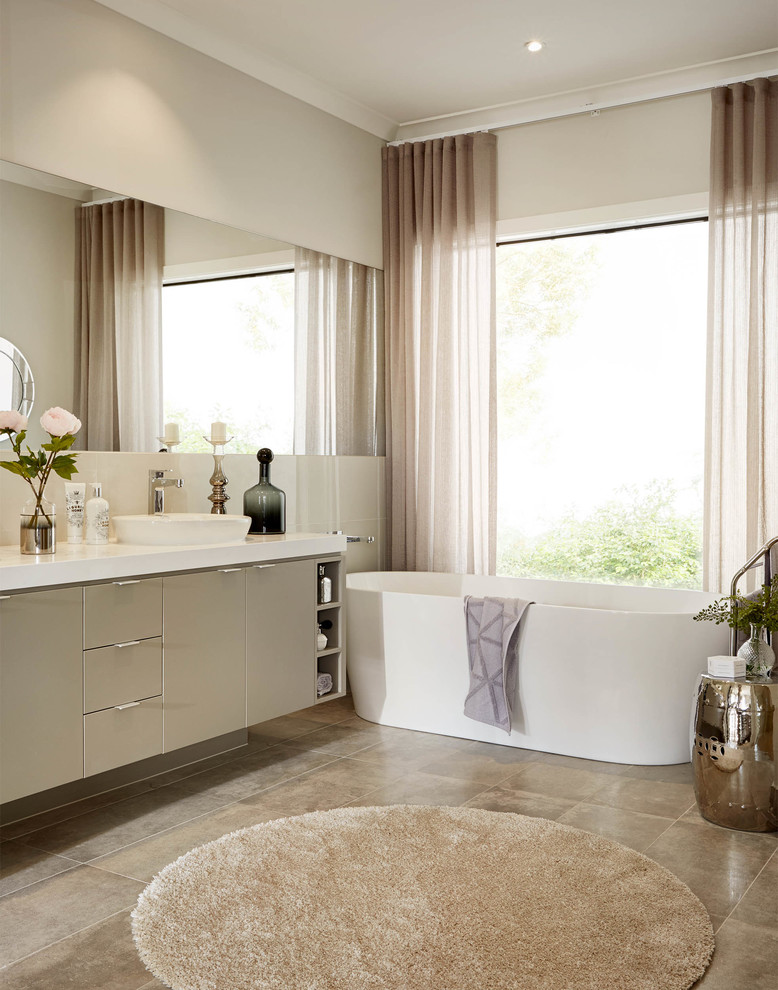 На фото: главная ванная комната в современном стиле с плоскими фасадами, серыми фасадами, отдельно стоящей ванной, бежевыми стенами и накладной раковиной с