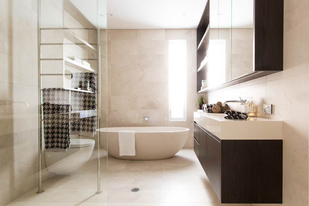 Пример оригинального дизайна: ванная комната среднего размера в современном стиле с плоскими фасадами, темными деревянными фасадами, отдельно стоящей ванной, открытым душем, унитазом-моноблоком, бежевой плиткой, плиткой из известняка, бежевыми стенами, полом из известняка, монолитной раковиной, бежевым полом и открытым душем