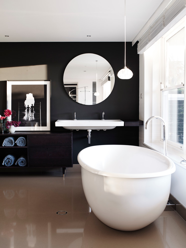 На фото: ванная комната в современном стиле с подвесной раковиной, отдельно стоящей ванной и черными стенами с