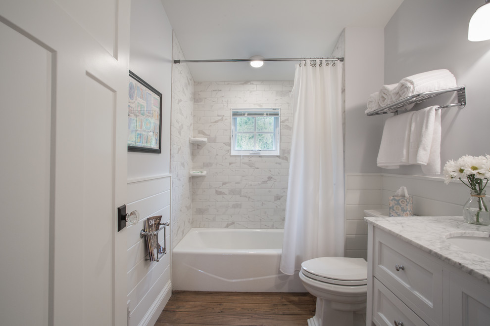Inredning av ett klassiskt mellanstort badrum, med luckor med infälld panel, vita skåp, ett badkar i en alkov, en dusch/badkar-kombination, grå kakel, tunnelbanekakel, grå väggar, mellanmörkt trägolv, ett undermonterad handfat, marmorbänkskiva, brunt golv och dusch med duschdraperi