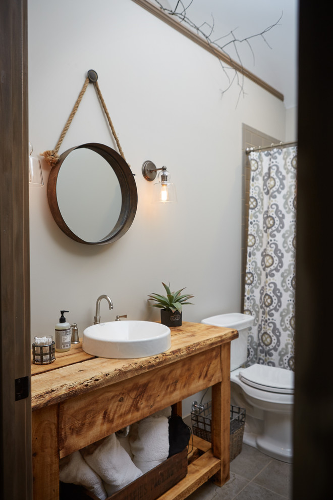 Rustic ensuite bathroom in Grand Rapids with a submerged sink, flat-panel cabinets, medium wood cabinets, granite worktops, a freestanding bath, an alcove shower, beige tiles, porcelain tiles, beige walls and ceramic flooring.