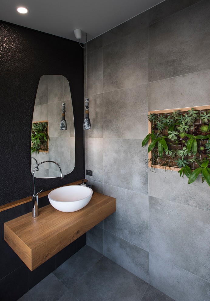 Foto på ett funkis brun badrum med dusch, med grå kakel, svart kakel, keramikplattor, klinkergolv i keramik, ett fristående handfat, träbänkskiva, grått golv och svarta väggar