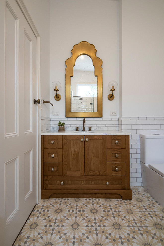 Идея дизайна: большая главная ванная комната в средиземноморском стиле с фасадами островного типа, фасадами цвета дерева среднего тона, ванной на ножках, белой плиткой, керамической плиткой, мраморной столешницей, белой столешницей, угловым душем, унитазом-моноблоком, белыми стенами, полом из цементной плитки, врезной раковиной, желтым полом и открытым душем