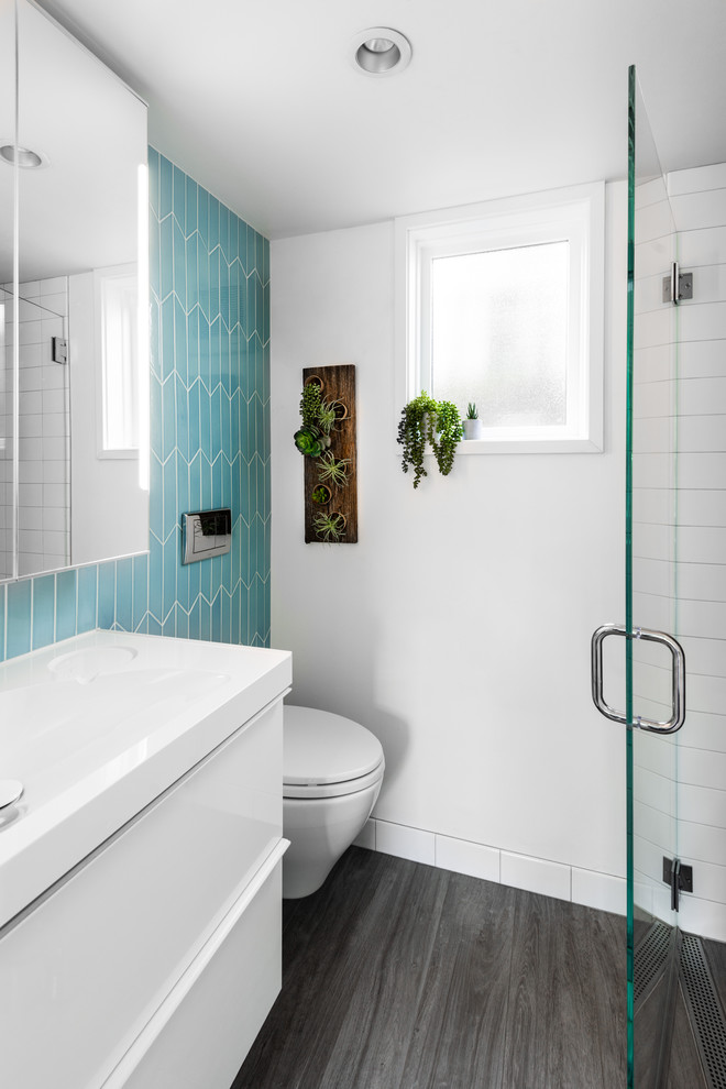 Foto på ett litet funkis vit badrum med dusch, med släta luckor, vita skåp, en dusch i en alkov, en vägghängd toalettstol, blå kakel, keramikplattor, vita väggar, ett integrerad handfat, bänkskiva i akrylsten, grått golv och dusch med gångjärnsdörr