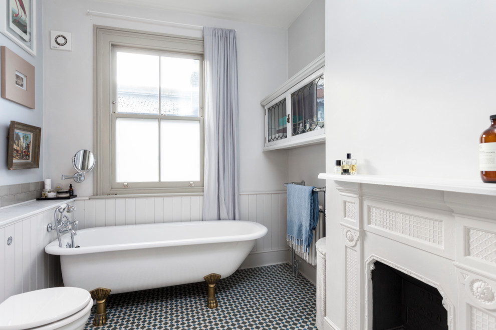 Photo of a scandinavian bathroom in London with a claw-foot bath, white walls, mosaic tile flooring, white cabinets and a chimney breast.