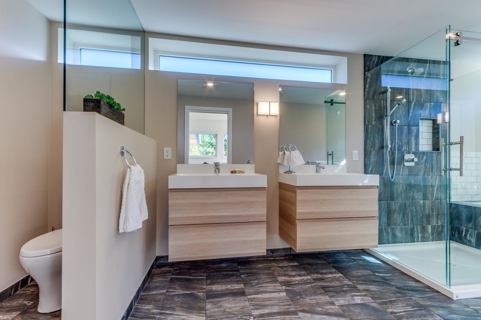 Cette image montre une grande salle de bain principale design en bois clair avec un placard à porte plane, une baignoire en alcôve, une douche d'angle, WC à poser, un mur beige, un sol en carrelage de céramique, un lavabo encastré et un plan de toilette en surface solide.