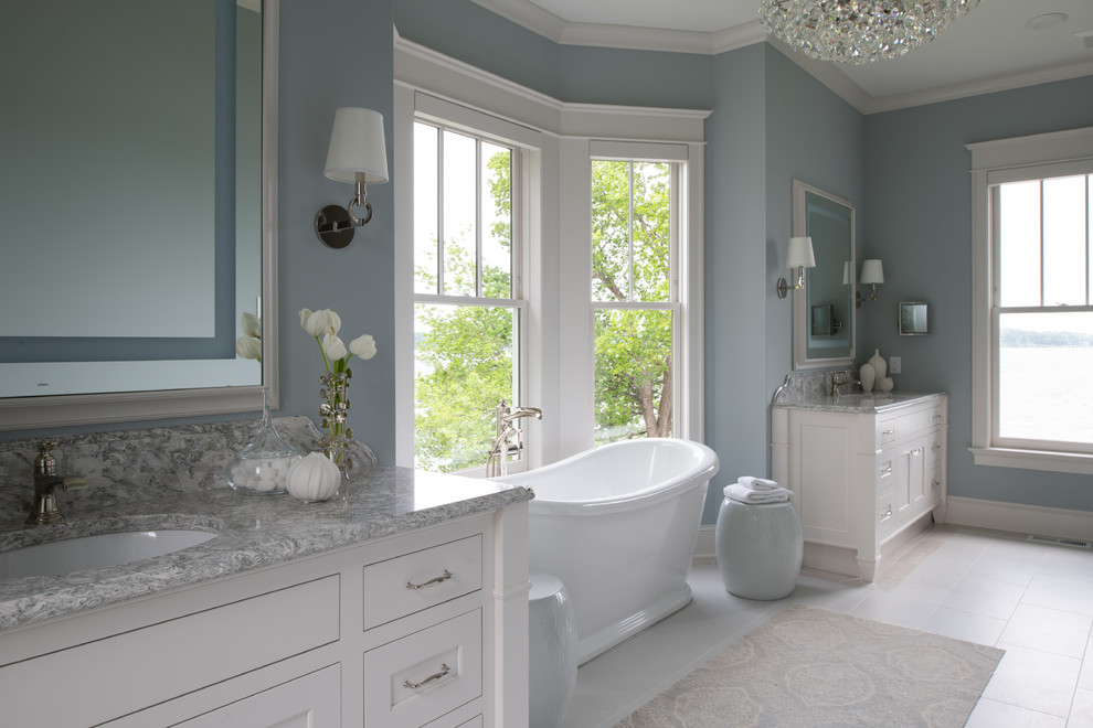 Idée de décoration pour une grande salle de bain principale tradition avec un placard à porte shaker, des portes de placard blanches, une baignoire indépendante, un mur bleu, un sol en carrelage de porcelaine, un lavabo encastré, un plan de toilette en granite, un sol blanc et un plan de toilette gris.