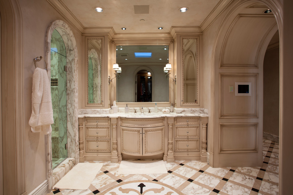 Mediterranes Badezimmer mit beigen Schränken, beigen Fliesen, beiger Wandfarbe, Unterbauwaschbecken, buntem Boden, Falttür-Duschabtrennung, weißer Waschtischplatte und profilierten Schrankfronten in Orange County